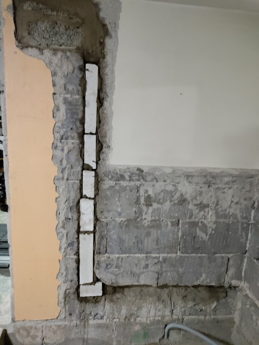 Vägg under renovering med exponerade tegelstenar och delvis borttaget puts samt vertikal installationskanal.