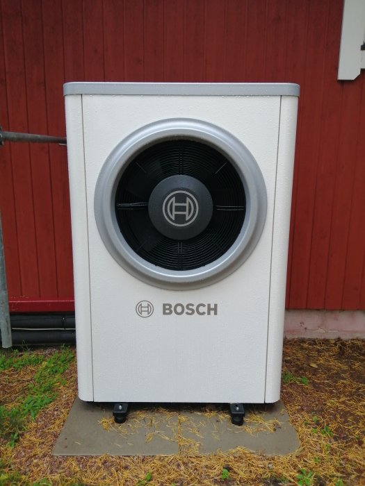 Bosch Compress 7000i AW 7 luft-vattenvärmepump på betongplattor med gummitassar och anslutna flexslangar.