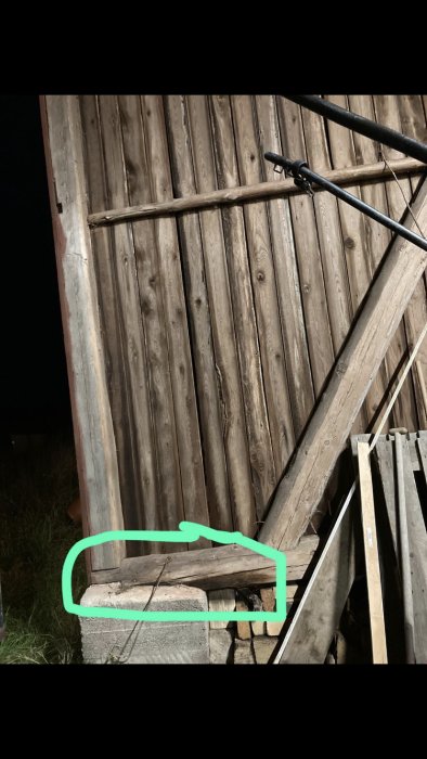 Murken träsyll som vilar på stenfundament med tecken på vattenskada, markerad med grön linje.