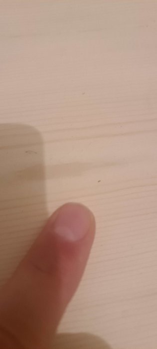 Finger som pekar på ett litet svart objekt på en ljus träyta för att visa objektets storlek.