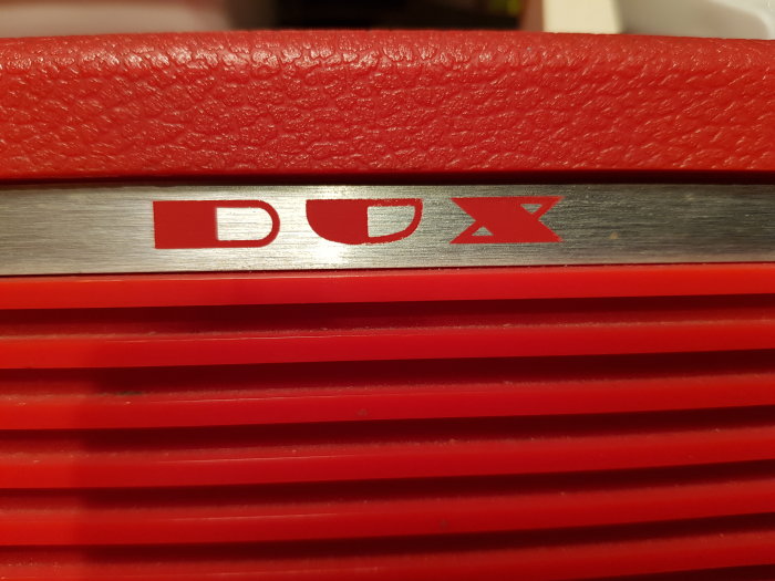 Röd bärbar skivspelare med märket "DOX" på metallinsatsen, från 1972, pickup saknas.