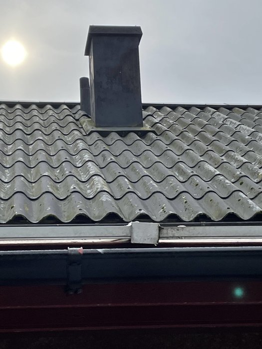 Ett vågformat tak med en skorsten mot en disig himmel och solen som skiner svagt.