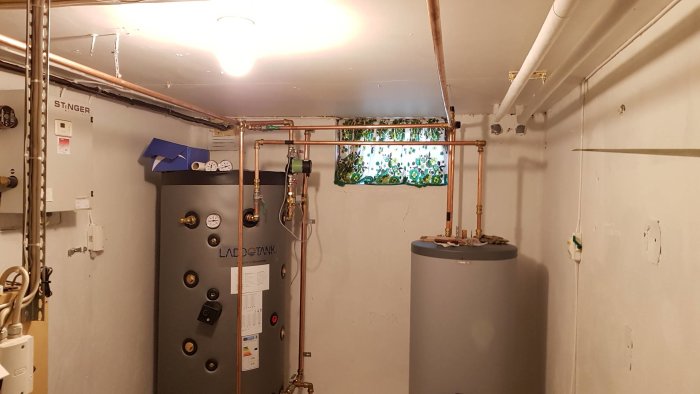 Ackumulatortank och varmvattenberedare med kopplade kopparrör i ett pannrum.