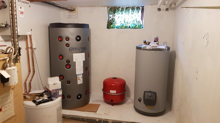 Installation av ackumulatortank och varmvattenberedare med kopplade rör i ett pannrum.