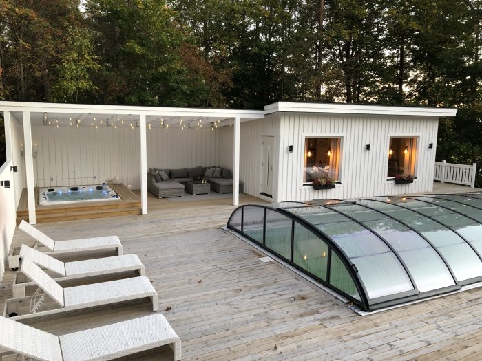 Renoverad altan med spabad under pergola, utemöbler, och pool med överdrag omgiven av natur.