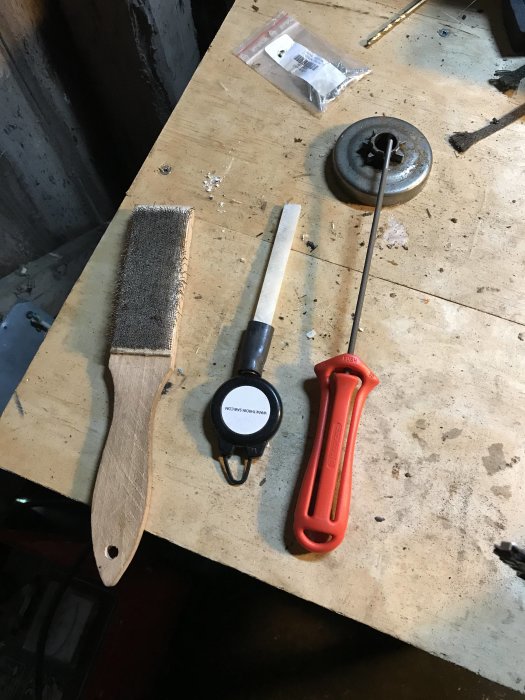 En filkarda, en rundfil med handtag, en rulle med krita och packade ersättningsdelar på ett arbetsbord.