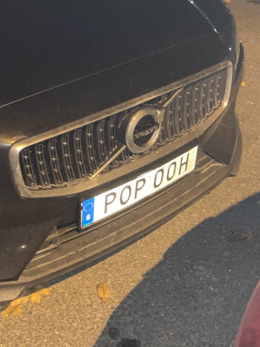 Svart Volvo bilfront med registreringsskylt "POP 00H" och delvis skadad stötfångare.