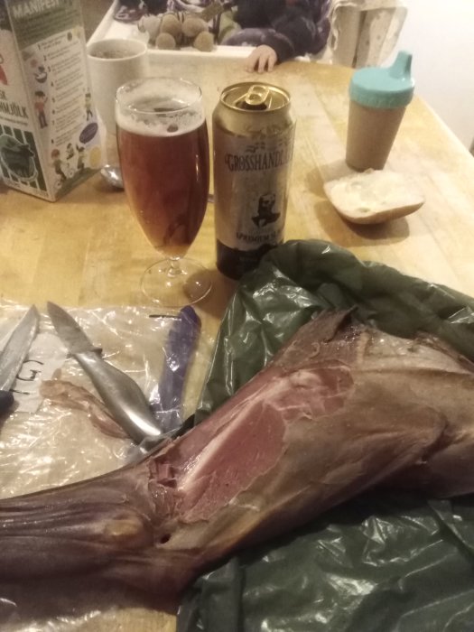Hemrökt rådjurslägg med en burk öl och ett glas på ett köksbord, omgivet av köksredskap och matrester.