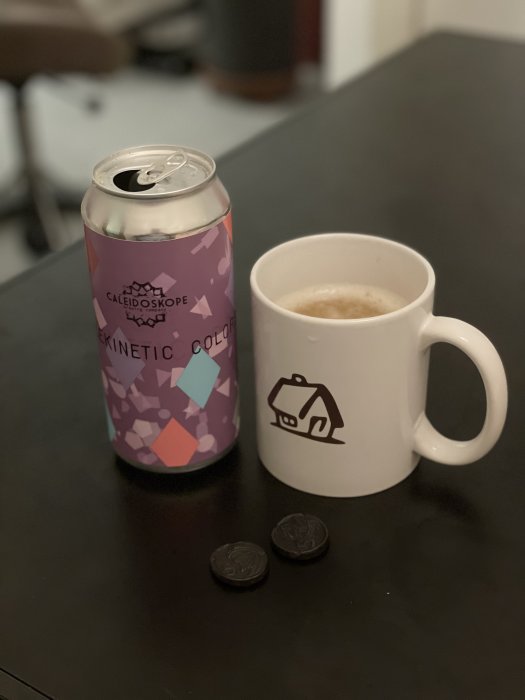 Ölburk med etikett "Harlekinetic Colors", kaffemugg med Byggahus-logotyp och två chokladbitar på bord.