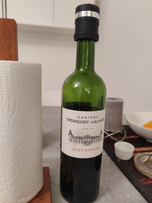 Vinflaska Château Tronquoy-Lalande 2014 på ett köksbord, beskriven som vass och tråkig trots dekantering.