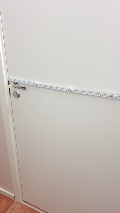 Måttband visar bredden på en vit dörr, vilket indikerar att man följer byggregler.