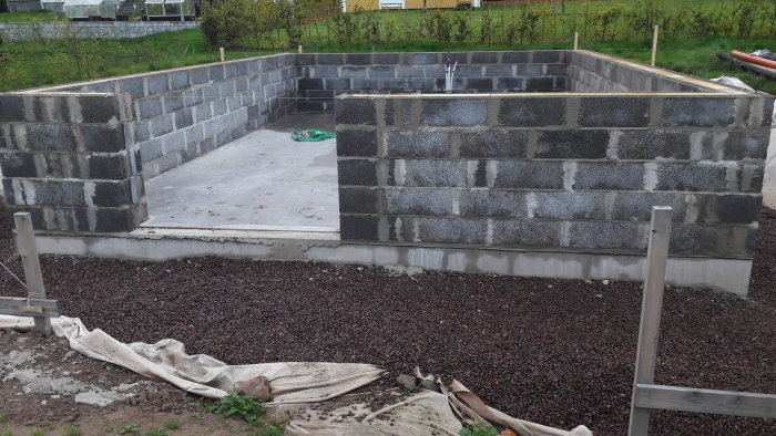 Nybyggd grå betongfundament med sista stenen på plats, omgiven av grus och staketstolpar.