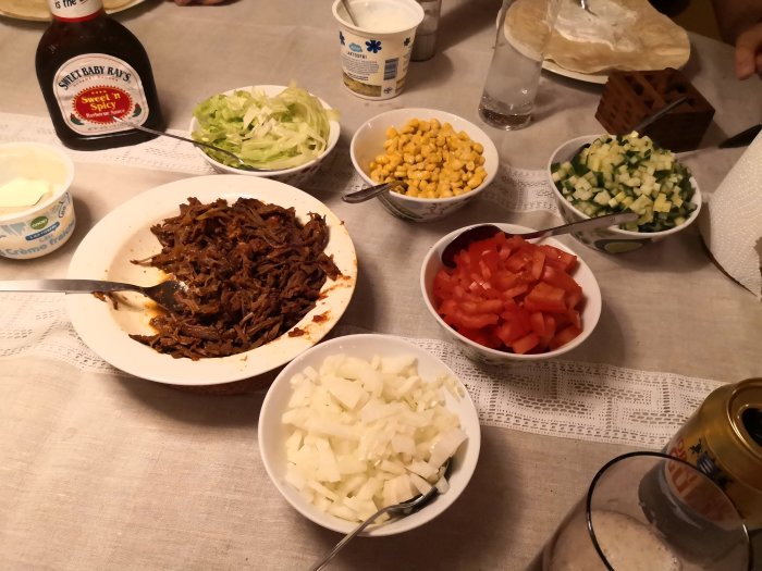 Bord med rätter inklusive pulled beef, hackad tomat, gurka, majs, lök, gräddfil och barbecuesås redo för taco-kväll.