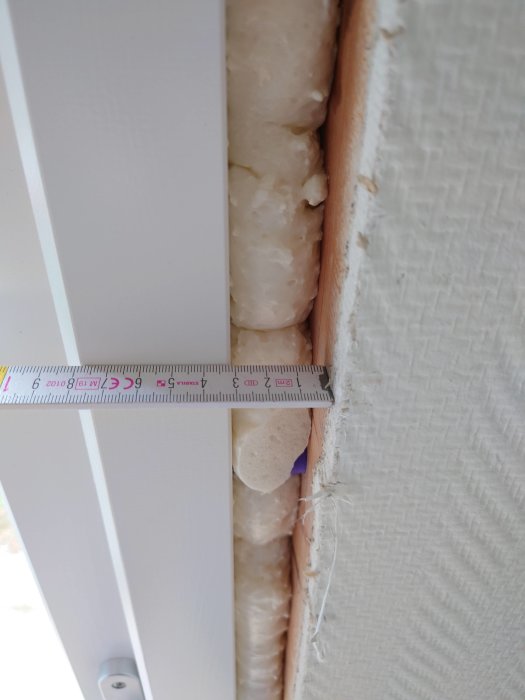 Mätning av isoleringstjocklek mellan vägg och fönsterkarm med tumstock.