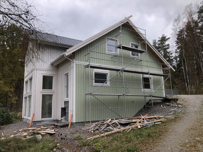 Hus under renovering med ställning och nymålad österfasad i ljusgrön, byggavfall framför.