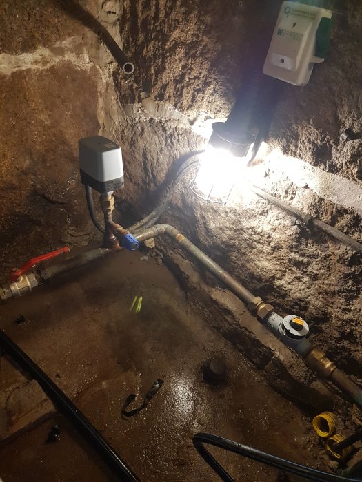 Ny tryckbrytare installerad på vattenpump i en grov källarmiljö med synliga rör och en lampa.