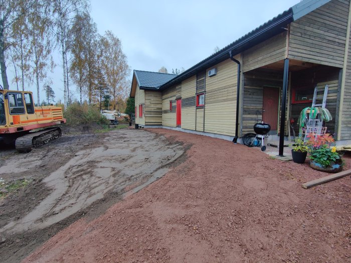 Nygrusad uppfart vid halvfärdigt hus med grävmaskin och husfasad i bakgrunden.