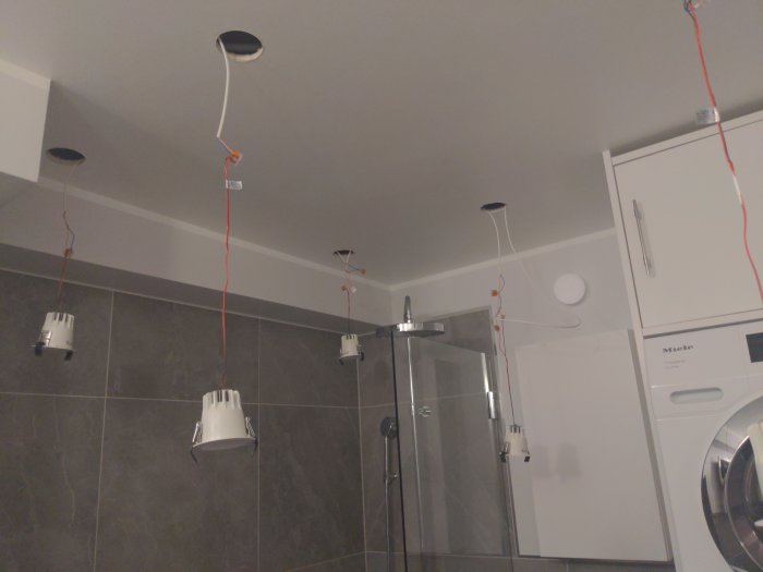 Badrum med sju LED-downlights hängandes från taket med synliga ledningar vid sidan av tvättmaskin och torktumlare.