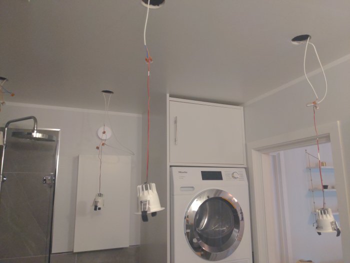 Oupphängda LED-taklampor bredvid tvättmaskin, en dold bakom tvättpelare.