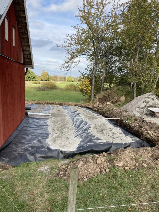 Glasfiberväv täcker mark vid ladugård för växtbekämpning, delvis täckt av stenmjöl, vid grävd dik.