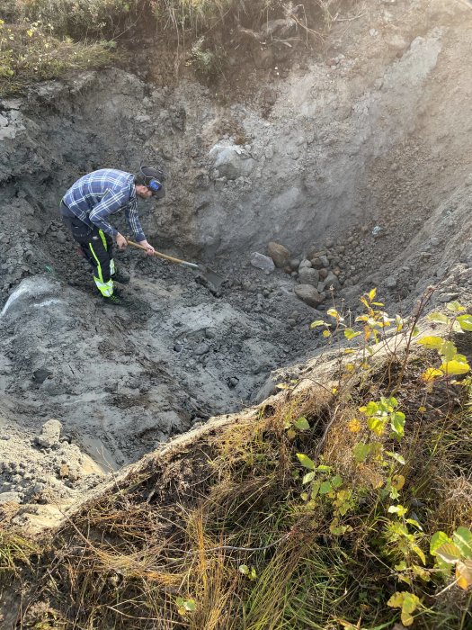 Person gräver i en grop för att ansluta avlopp och vatten i ett byggprojekt.