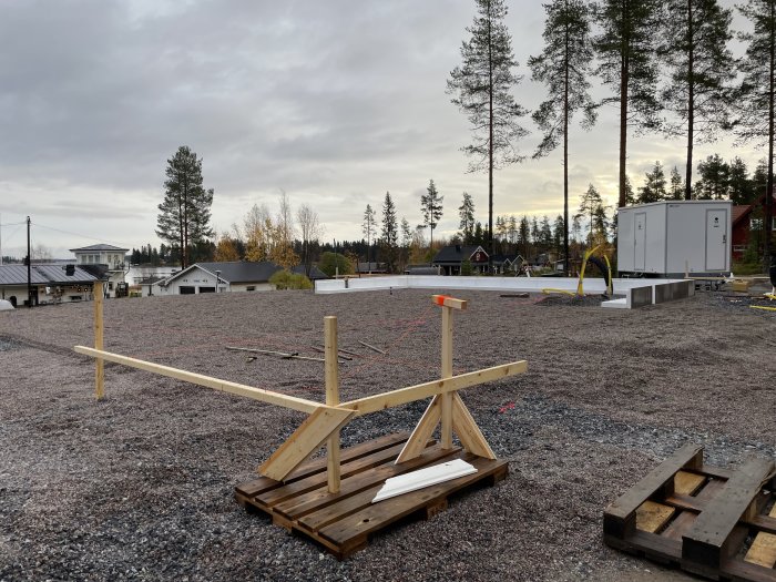 Byggarbetsplats med anslutningar för avlopp, vatten och el, samt kantbalk och isolering på grusmark.