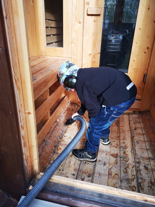 Barn använder en grovdammsugare för att städa i en bastutunna av trä.