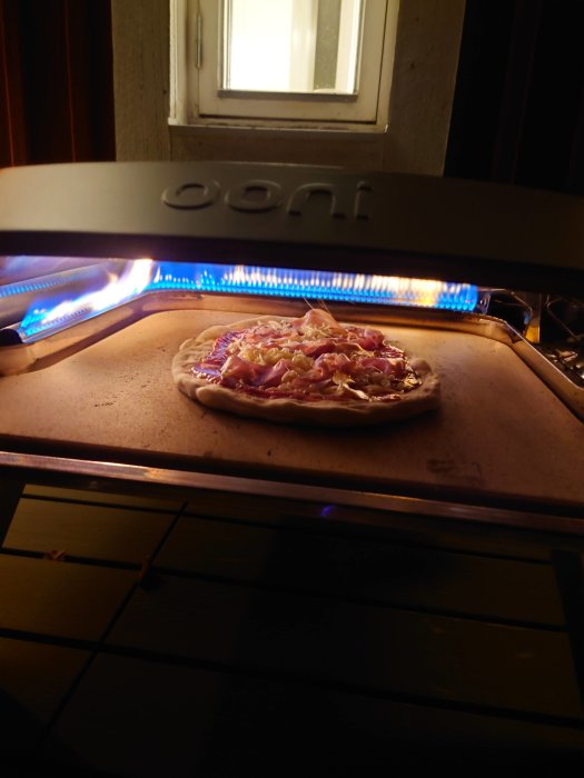 Pizza med tonfisk, salami, lök och ananas i en bakugn.