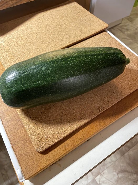 Stor grön squash ligger på en korkskärbräda i ett kök.