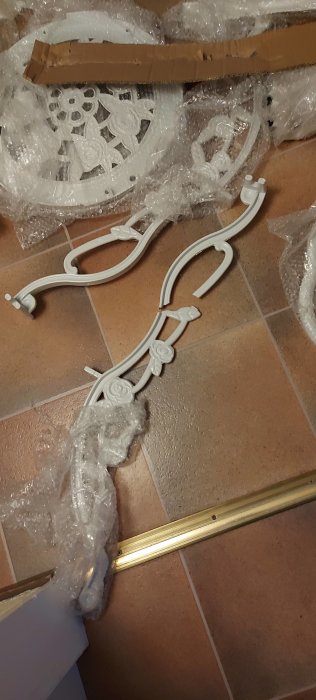 Vit metallmöbeldel på golv med skyddande bubbelplast, skadad och behöver lagning.