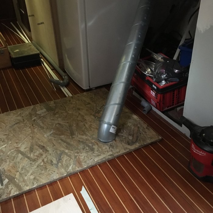 Böjt metallrör på golvet i ett rörigt utrymme med verktyg och byggmaterial.