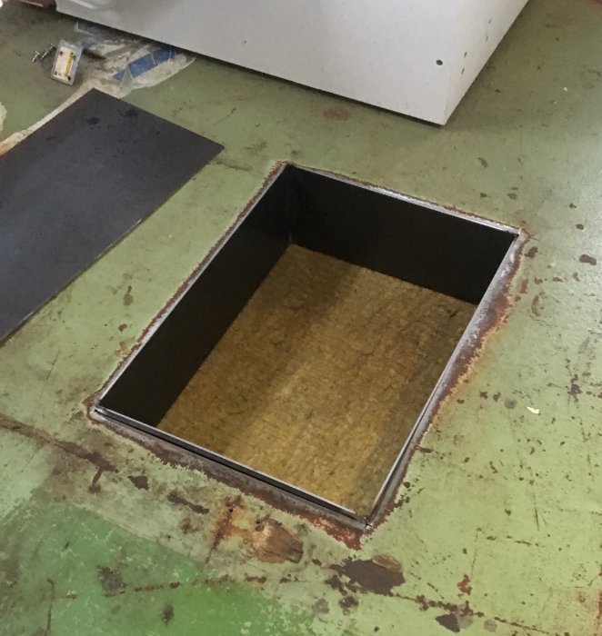 Metallram installerad i golv, visar öppning och foderramen anpassad mot markskivan i en verkstadsmiljö.