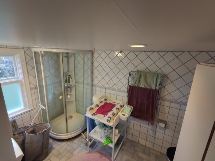 Ett badrum med vita kakelväggar, duschhörn med glasdörrar och varierande badrumstillbehör.