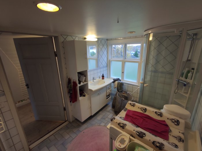 Badrum med vit inredning, duschkabin, handfat och badrumsskåp, samt rosa matta och handdukar.