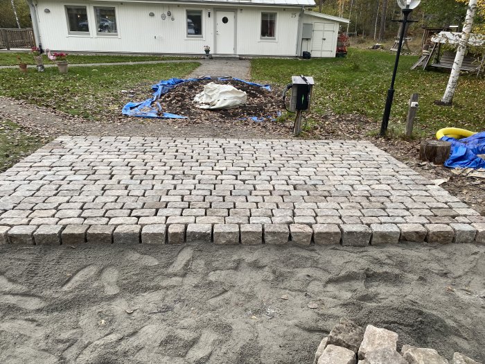 Ny lagd gångväg av återanvänd storgatsten i svensk granit framför ett hus.