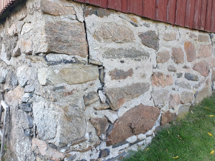 Gammal jordkällarvägg av oregelbundna stenar med synligt slitet och delvis eroderat murbruk.