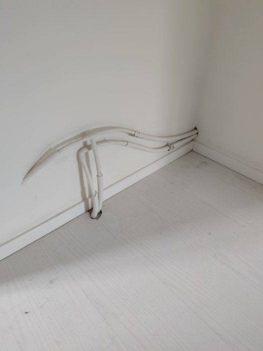 Vitklädda rör som är monterade längs hörnet av ett rum, dragna genom golvet och väggen i en knepig rördragning.