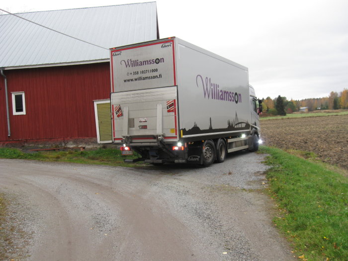 Lastbil från Williamssons parkerad på en grusväg bredvid ett rött lantbrukshus.