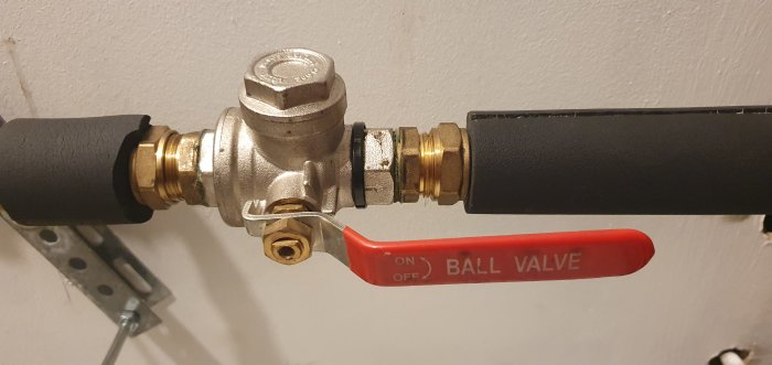 Ventil med röda handtaget märkt "BALL VALVE" inställt på OFF, kopplad till rör med isolering.