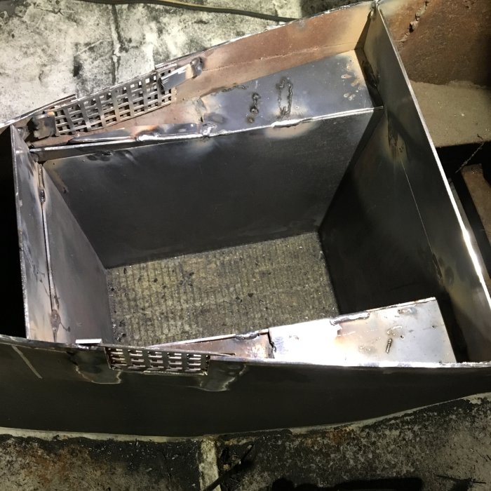 Vy underifrån av en svetsad metallkonstruktion, troligen en del av en kamininstallation, i ett byggprojekt.