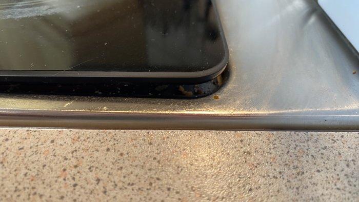 Närbild på en spishäll som behöver reparation, med synligt silikon och gamla rester vid kanten.