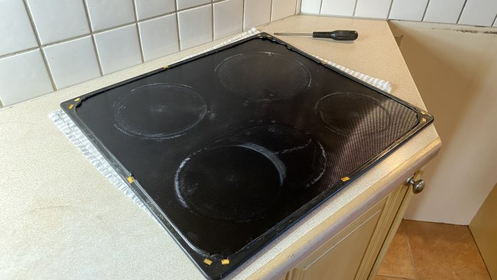 Svart häll av glaskeramik med ram lyft och torkat silikon synligt, vid reparation.