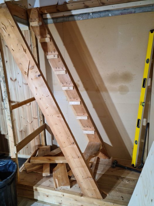 Nybyggd trätrappa under konstruktion i oavslutat utrymme med verktyg och byggmaterial.