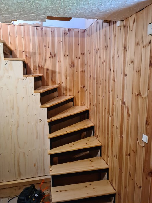 Nybyggd trätrappa i ett rum med träpanelväggar och osatt sättsteg.
