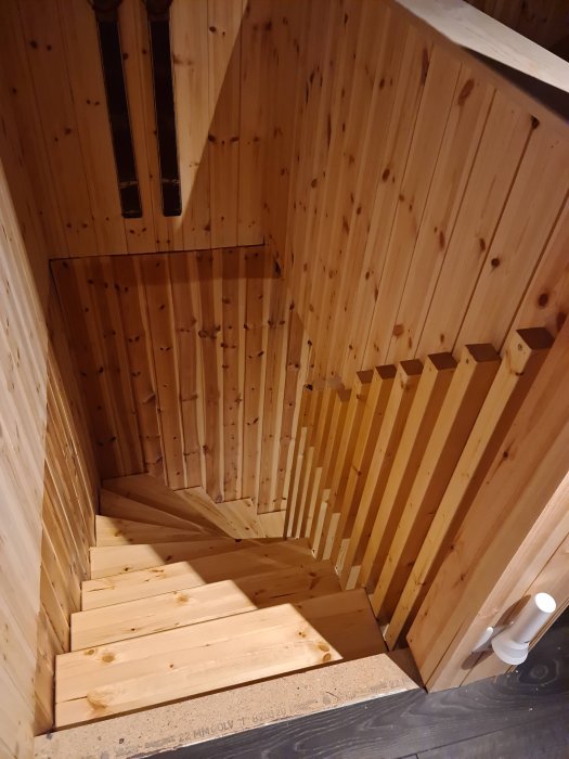 Nybyggd trätrappa inomhus med öppna steg och omålade träsättsteg och panelväggar samt oavslutad nedervåning.