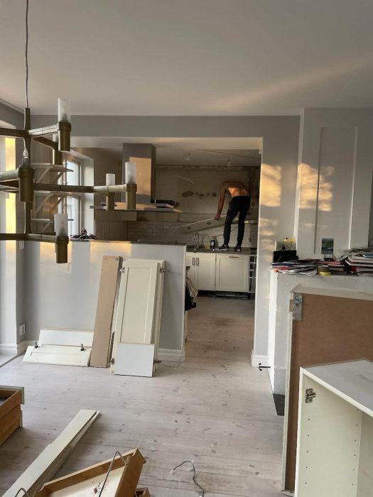 Person demonterar köksskåp i ett kök under renovering med borttagna luckor på golvet.