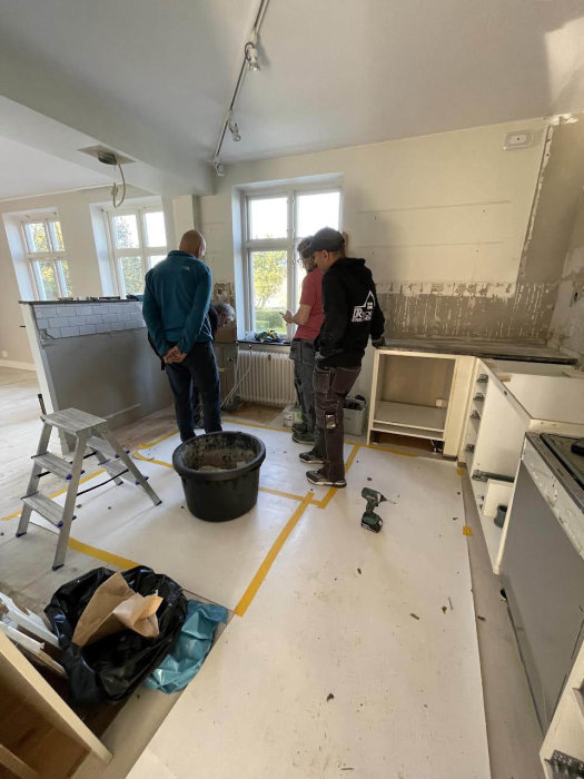 Två personer bedömer renoveringsarbete i ett kök med demonterade skåp och radiator.