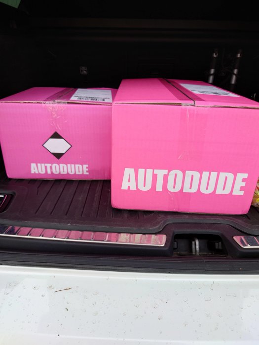 Två rosa AUTODUDE-lådor i bagageutrymmet på en bil.