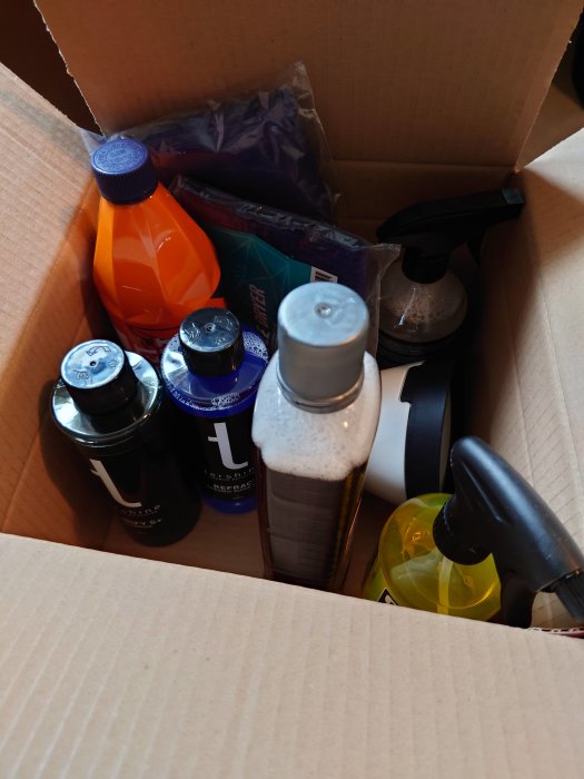 Kartong med olika produkter för rengöring och underhåll, inklusive sprejflaskor och plastflaskor.