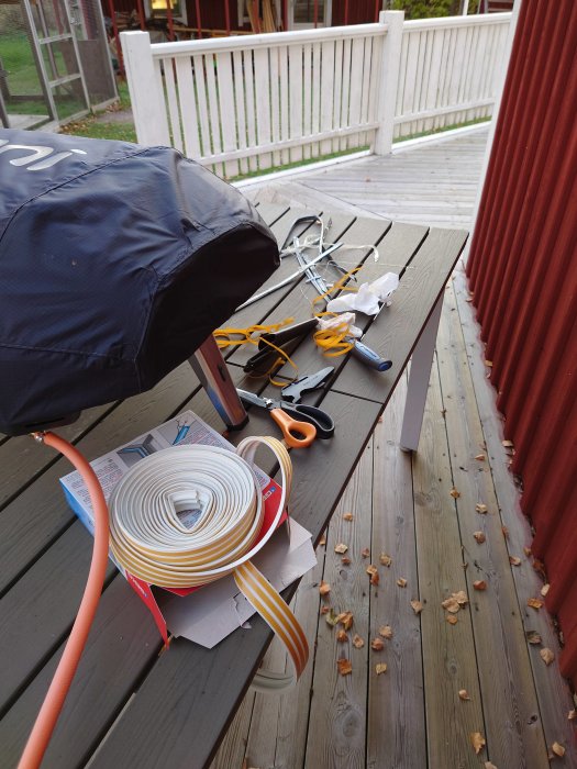 Verktyg och tätningslister på ett träbord utomhus, förberedelse för byte av köksfönstertätning.